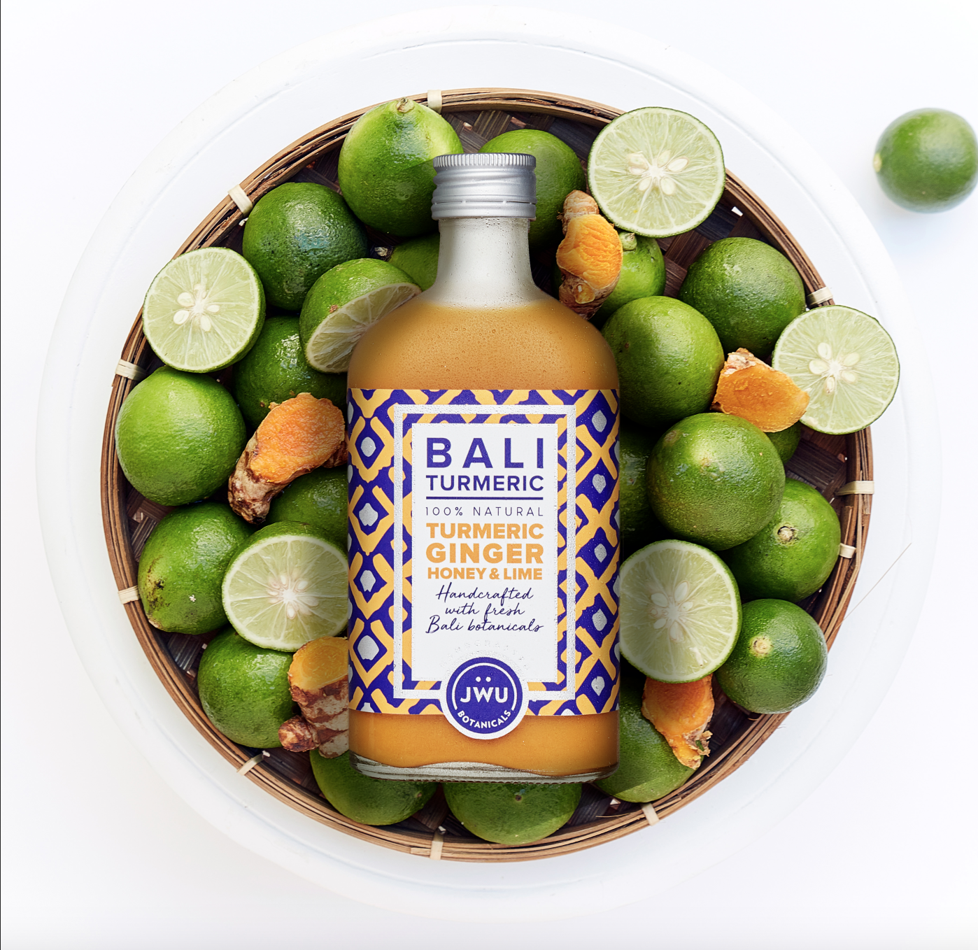 Turmeric jamu bottle with fresh Bali limes and turmeric roots in a bamboo basket